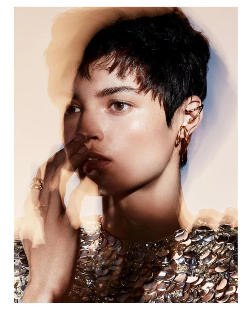 Close-up of a stylish adult woman with short brown hair, wearing gold jewelry and a sequined top, posing in a photo studio.