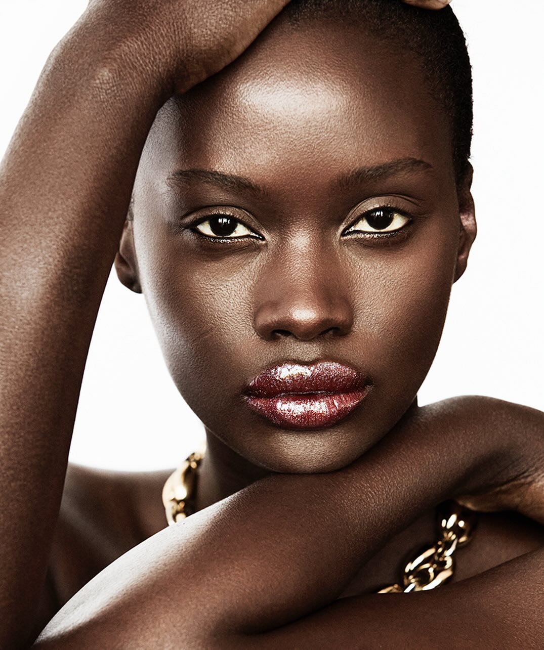 Close-up beauty portrait of a Black woman with glossy lips and gold chain necklace against a white background