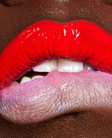 Close-up of red and pink glossy lips with teeth visible, dark skin tone, beauty shot emphasizing makeup and detail, with a focus on texture.