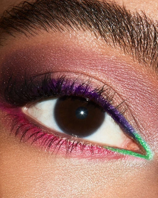 Close-up of an adult female eye with pink and purple eyeshadow and green eyeliner. Focus on colorful makeup and eyebrow details.