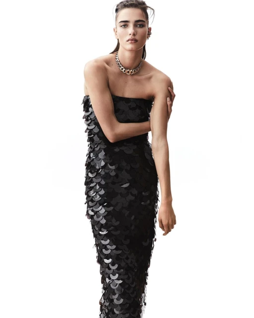 Elegant woman in black strapless sequin gown with chain necklace posing against a white background in a studio fashion shot.