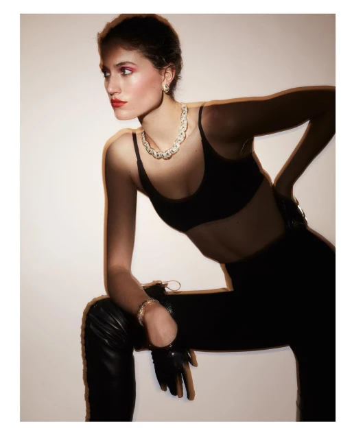 Woman in black outfit and jewelry posing in front of a white background in a studio. She is wearing a necklace, earrings, and bracelets.