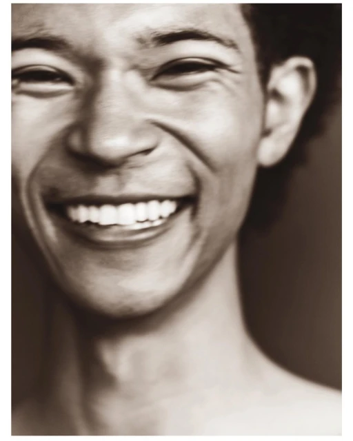 Close-up portrait of a smiling Asian man with fair skin showing his teeth, against a blurred sepia-toned background.