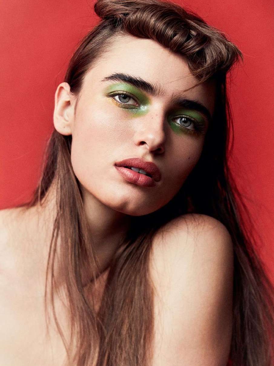Portrait of a beautiful woman with brown hair and green eyeshadow against a red background. Beauty and fashion editorial portrait.