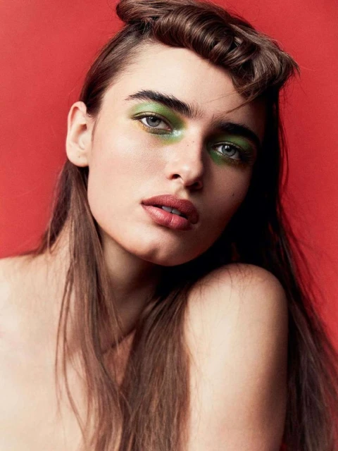 Portrait of a beautiful woman with brown hair and green eyeshadow against a red background. Beauty and fashion editorial portrait.