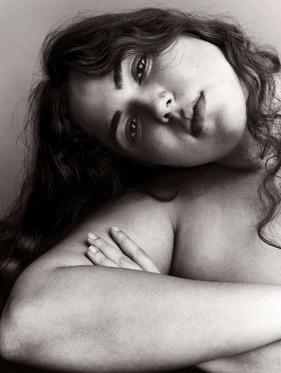 Black and white portrait of an adult woman with long, dark curly hair gazing forward with her arms crossed in front of her body.
