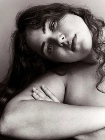 Close-up monochrome portrait of a woman with long dark wavy hair leaning with crossed arms by Mikael Schulz