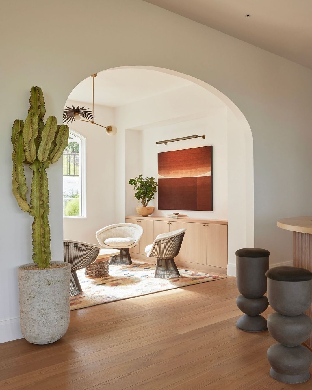 Living room interior with a tall cactus in a pot, arched doorway, neutral furniture, modern lighting, and wooden floor creating a warm, inviting space.