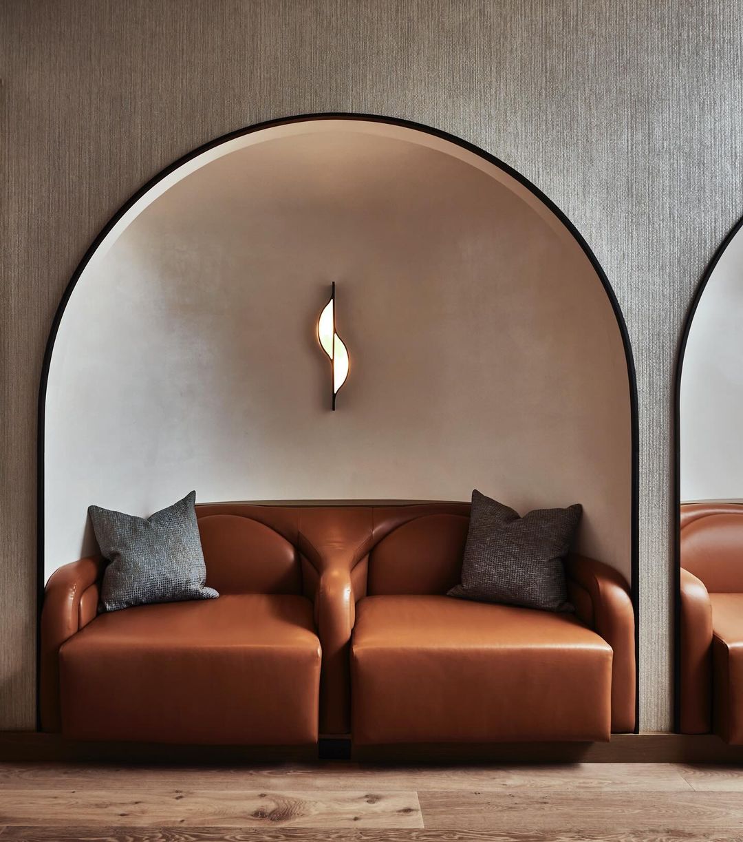 Modern interior with a tan leather sofa and gray pillows set against a textured gray wall with a black arched frame.