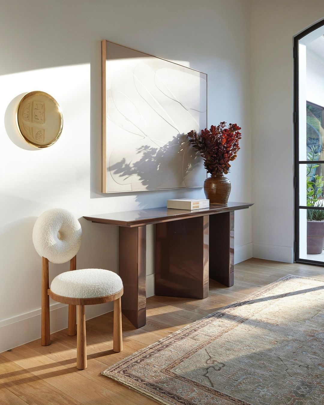 Interior shot featuring a decorative chair, brown console table adorned with a vase and a modern art painting, and a patterned rug.