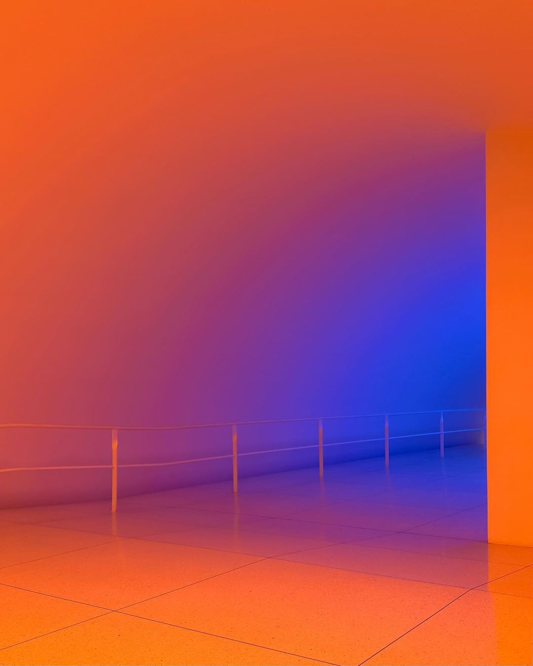Abstract architectural space featuring a corridor with blue and orange lighting and a guard rail, emphasizing color and form.