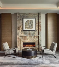 Modern living room interior with a marble fireplace, round coffee table, two armchairs, and framed art by photographer Mike Schwartz.