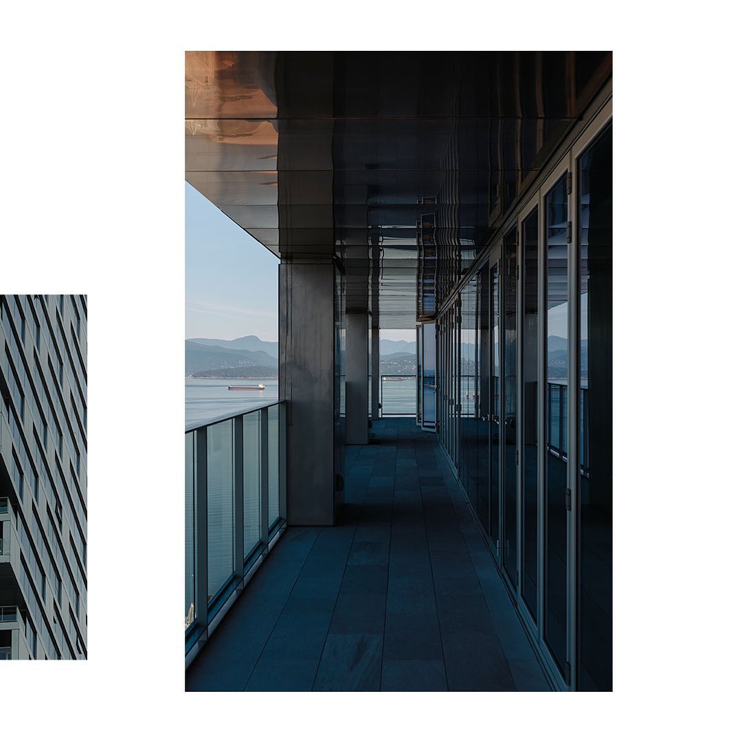 Exterior of modern high-rise building with glass balcony overlooking water and mountains on a clear day, architectural photography.