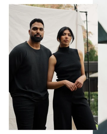 Portrait of a South Asian man and woman in black apparel standing together against a white fabric backdrop.