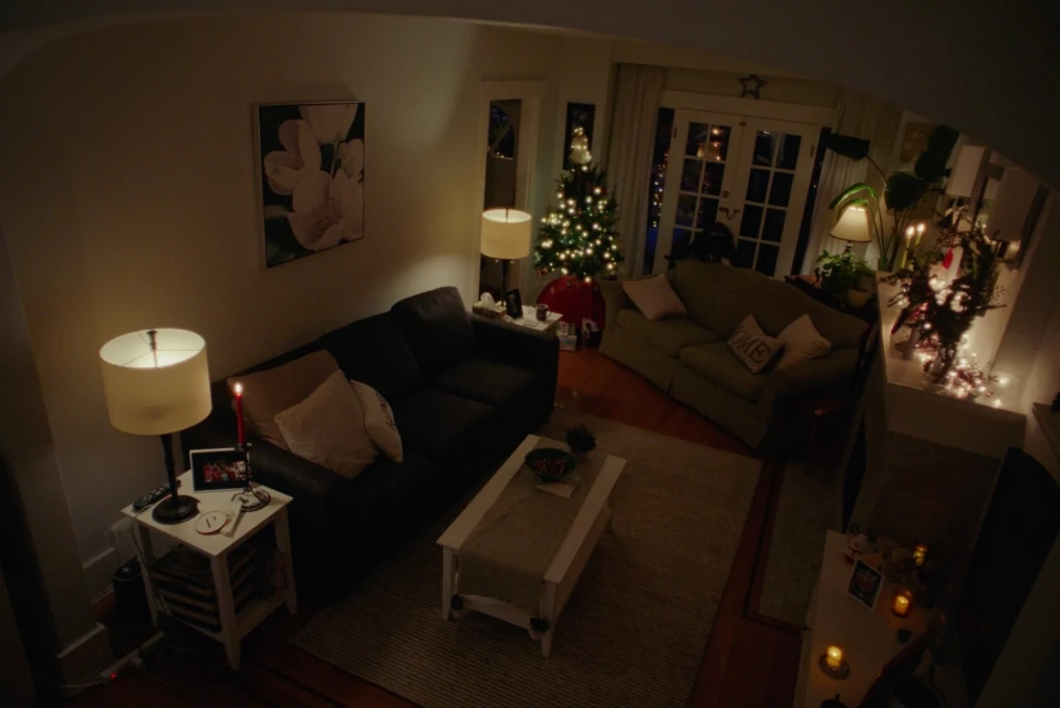 Cozy living room decorated for Christmas with a lit tree, couches, a white coffee table, and warm ambient lighting.