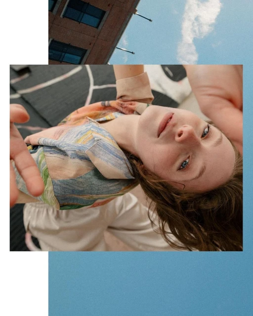 Eye-level shot of a relaxed, fair-skinned young woman with blue eyes. She is wearing a patterned shirt against a blue sky background.