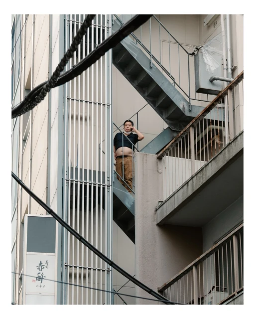 Adult man on a metal stairwell of an apartment building talking on a cell phone while standing on the balcony in an urban setting.