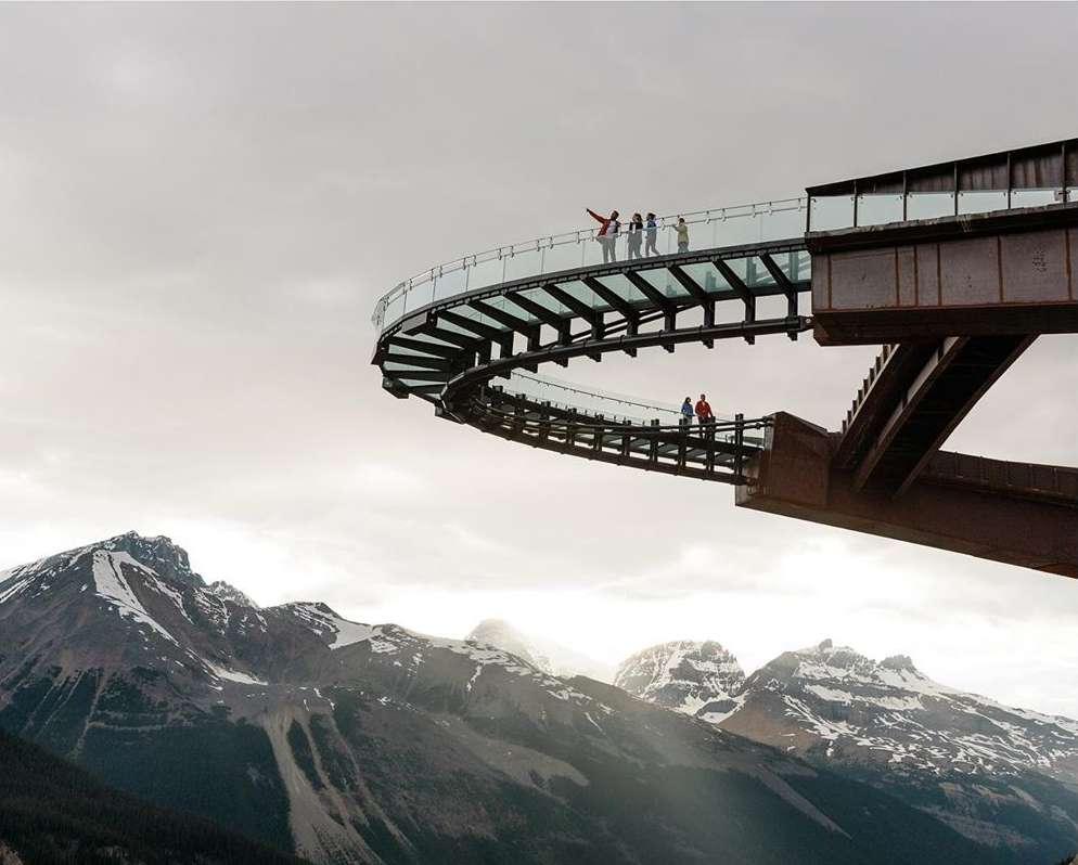 People on the observation deck overlook the snow-capped mountains under a cloudy sky, providing a scenic travel destination.