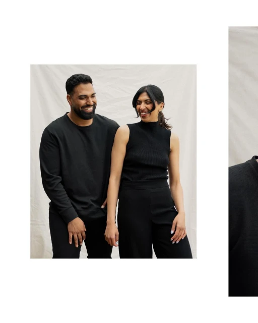 Portrait of a smiling East Indian couple in black tops and pants against a cream-colored muslin backdrop, shot in a bright photo studio.