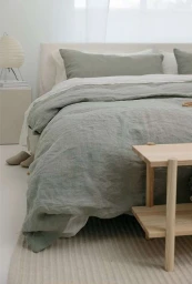 Minimalist bedroom with sage green linen bedding, light wood bedside bench, and soft neutral tones captured by Mike Seehagel