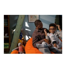 Black father and son relaxing together on an orange beanbag chair in a childs bedroom.
