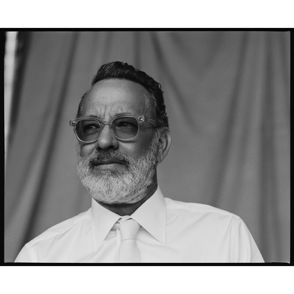 Black and white portrait of an adult male with glasses, a beard, and a white shirt and tie in front of a draped backdrop.