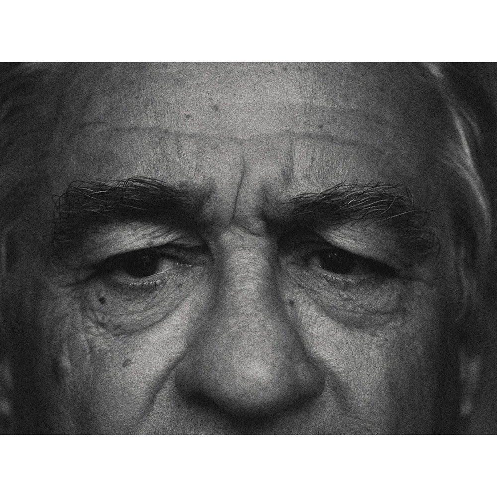 A black and white close-up photograph captures the intense gaze of an older adult male, focusing on his eyes, eyebrows, and wrinkled forehead.