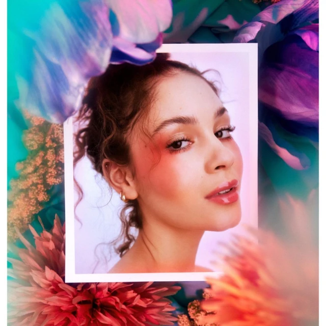 Portrait of a woman with a red blush framed by a white border, surrounded by turquoise and red flowers, eye-level angle and studio lighting.