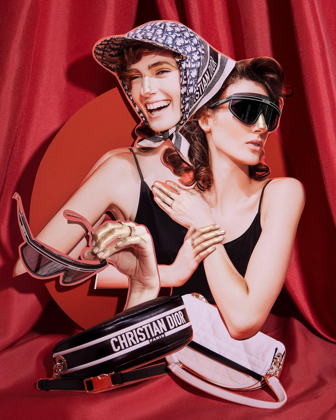 Two women pose in a fashion-forward composition with Christian Dior handbags, sunglasses, and a headscarf against a red curtain backdrop.