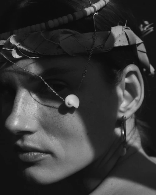 Close-up black and white portrait of a woman wearing a shell necklace and a woven headpiece, showcasing fashion and beauty.