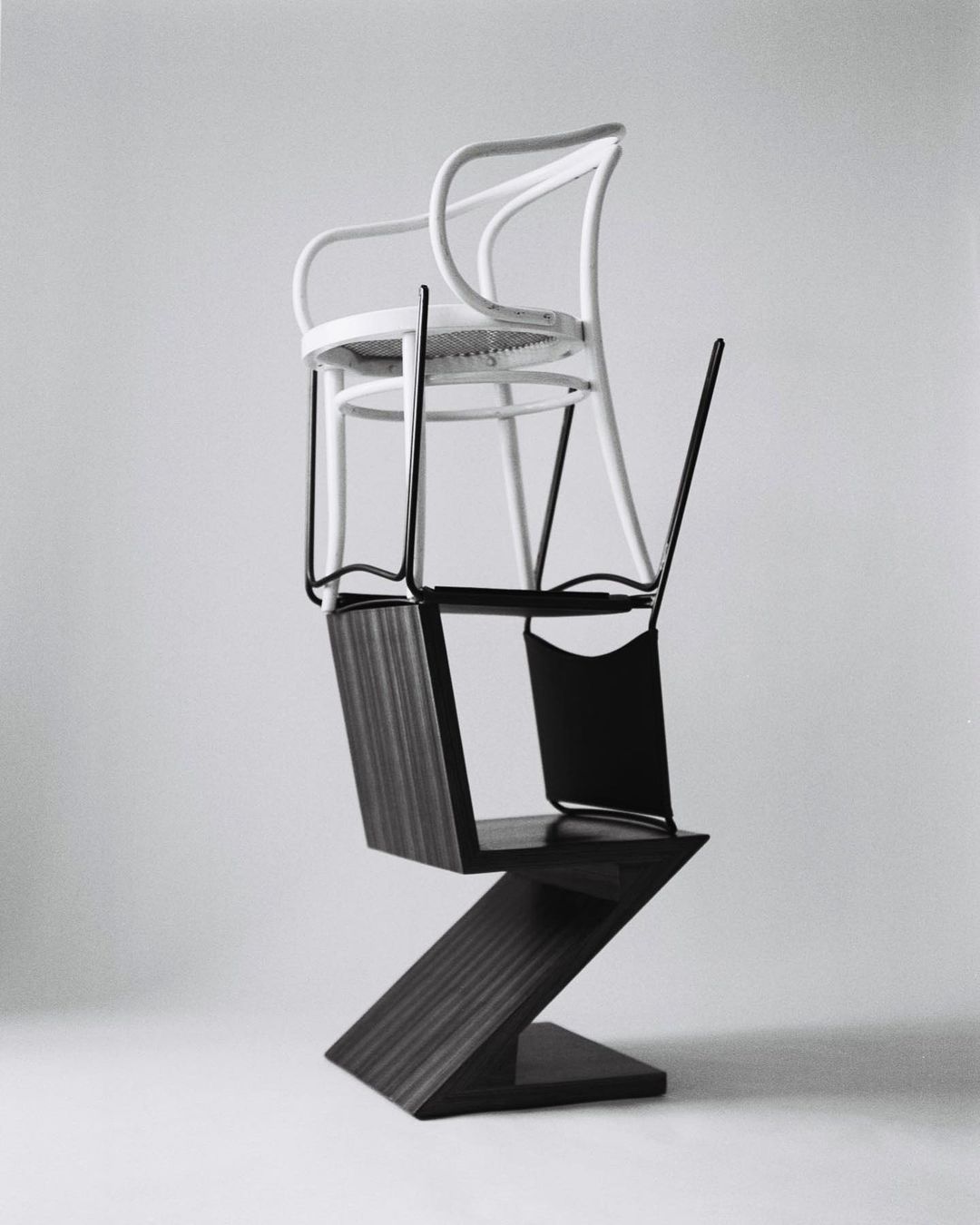Three chairs stacked on top of each other in a photo studio. The chairs are various shapes, styles, and colors on a grey background.