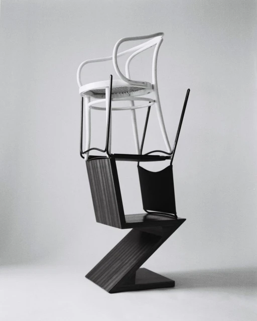 Three chairs stacked on top of each other in a photo studio. The chairs are various shapes, styles, and colors on a grey background.