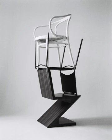 Three chairs stacked on top of each other in a photo studio. The chairs are various shapes, styles, and colors on a grey background.