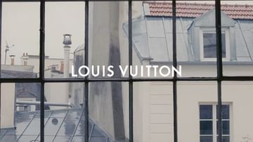 Louis Vuitton logo on a window overlooking a Parisian cityscape with rooftops and dormer windows on a cloudy day. 
