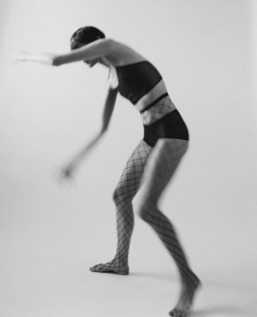 Black and white long exposure studio shot of a slender person with short hair, wearing lingerie and fishnet stockings, and a blurred body.