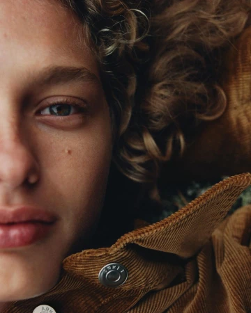 Extreme close-up portrait of a person with curly hair wearing a brown corduroy jacket shot by Misha Taylor.