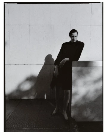 Model in dark clothing leaning against a tiled architectural wall with strong shadows by photographer Misha Taylor.