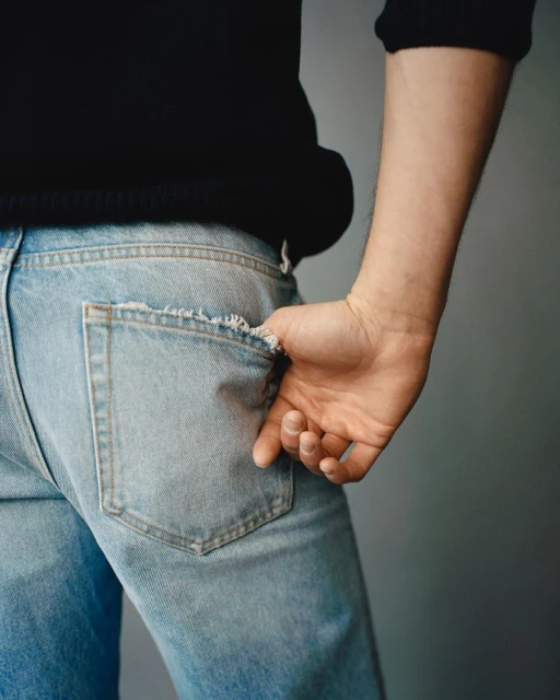 Close-up of a man's hand in the pocket of light-wash denim jeans, with a black sweater on a grey background, fashion.