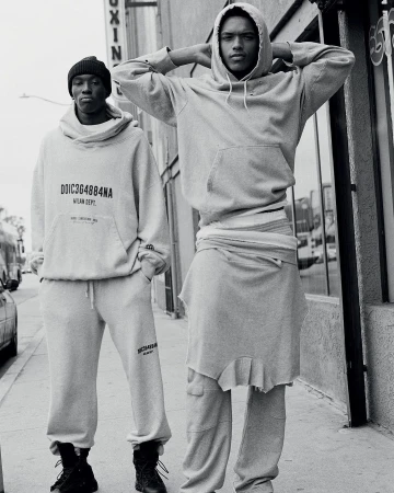 Two adult males wearing matching sweatshirts and sweatpants, photographed outdoors in black and white in an urban environment on a sunny day.