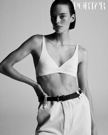 Monochrome portrait of a slender woman in a bra top and jeans, posing against a grey background, highlighting fashion and beauty.