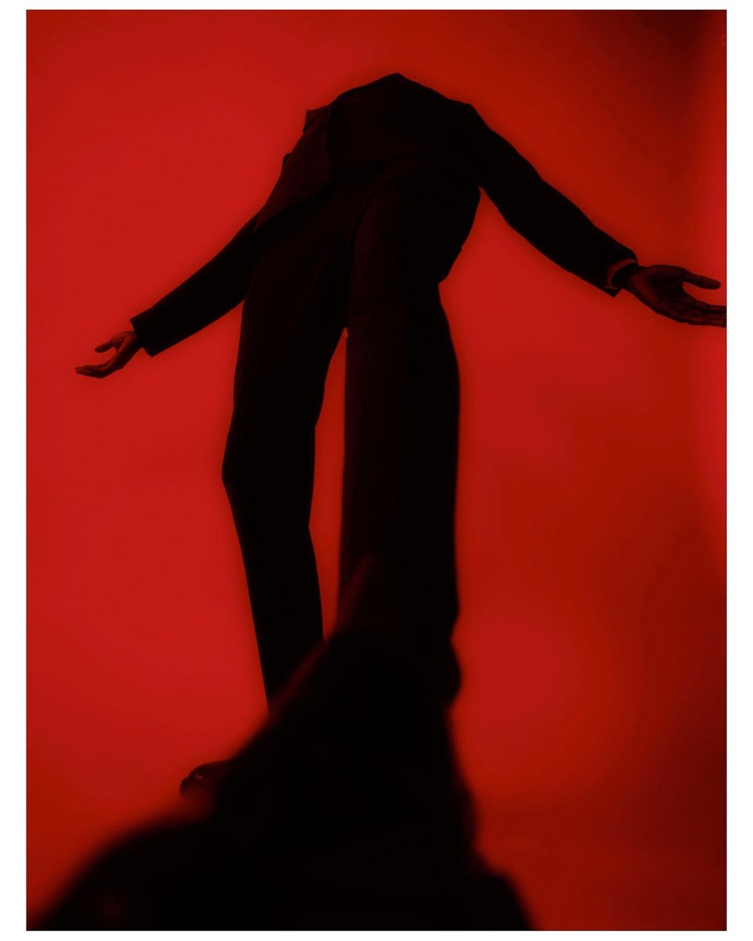 Full body photo of a person in a dark suit posing with arms outstretched on a red background. Fashion and posing concept.