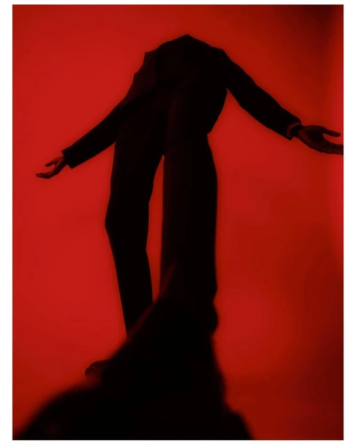 Full body photo of a person in a dark suit posing with arms outstretched on a red background. Fashion and posing concept.