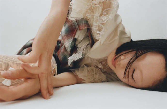 Close-up portrait of a woman in an ivory lace blouse and plaid skirt reclining on a plain white background by Misha Taylor.