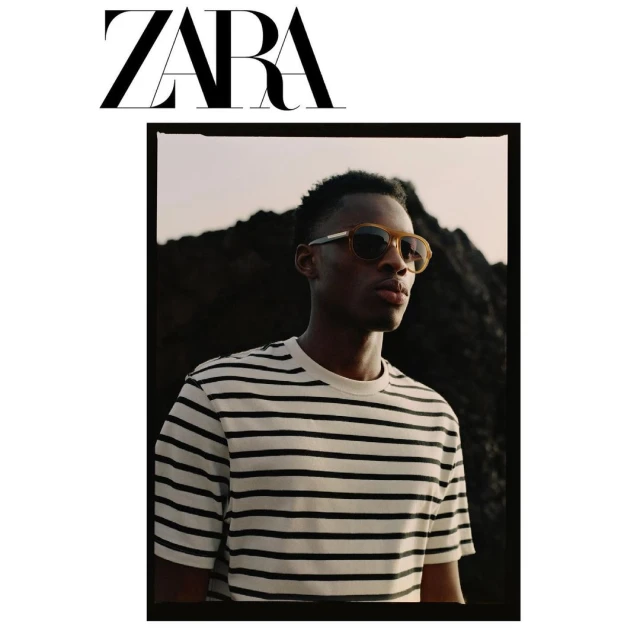 Zara brand advertisement of a Black male model wearing sunglasses and a striped shirt, photographed against a dark rocky backdrop.