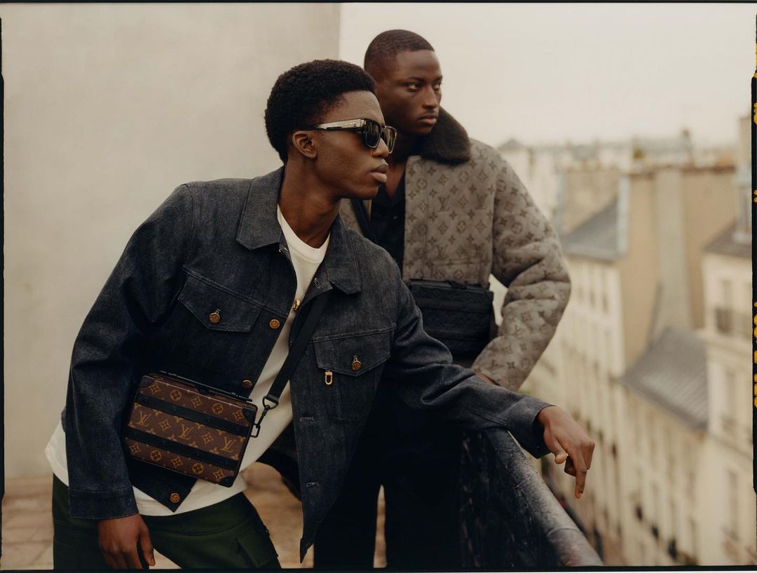 Two Black men in Louis Vuitton jackets stand on a rooftop in Paris with views of buildings in the background, fashion editorial.