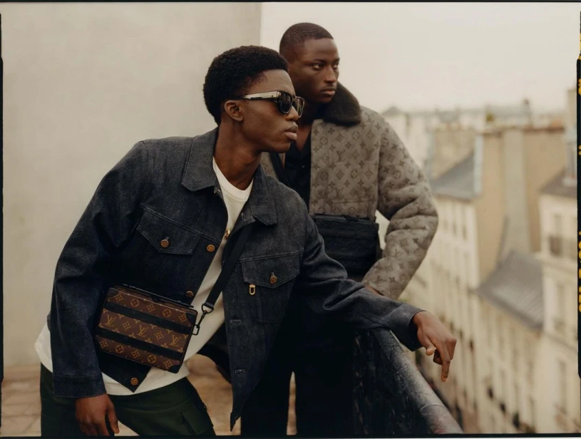Two Black men in Louis Vuitton jackets stand on a rooftop in Paris with views of buildings in the background, fashion editorial.