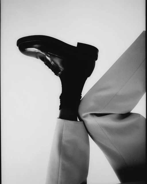 Fashion still life: a black leather dress shoe is prominently featured atop a pair of light-colored trousers and a black sock.