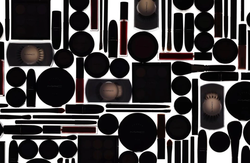 High-angle, full-frame product photography of a variety of MAC makeup products in black packaging on a white background, creating a seamless pattern.