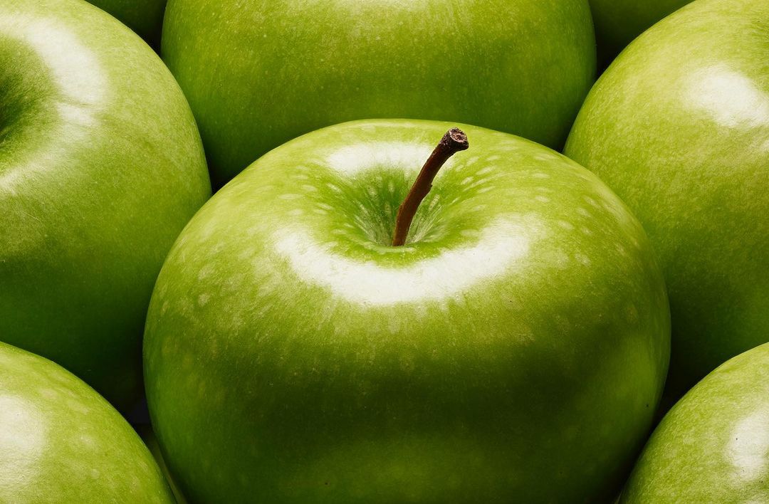 Close-up of green apples filling the frame, showcasing their vibrant color, textures, and stems, with a focus on freshness.