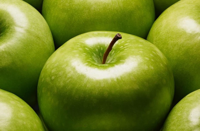 Close-up of green apples filling the frame, showcasing their vibrant color, textures, and stems, with a focus on freshness.
